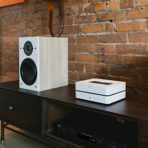Bluesound Vault 2i White on a redenza beside DALI Oberon Bookshelf Speakers in Light oak with an NAD C338