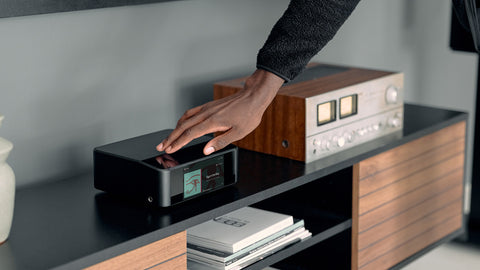 Hand reaching towards a Bluesound NODE Icon on a wooden cabinet.