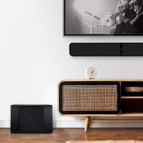 Bluesound Pulse Sub Plus Black on floor beside credenza