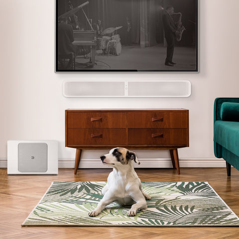 Bluesound Pulse Sub Plus White on the floor beside credenza that has a Pulse Soundbar Plus White mounted below a TV