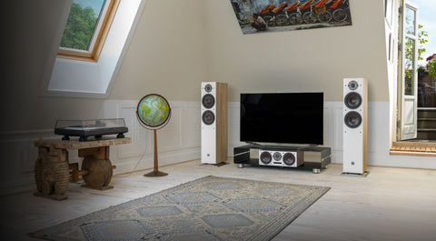 Home theater setup with DALI Oberon speakers, TV, and decorative items in a room with large windows.