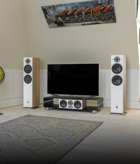 Home theater setup with DALI Oberon speakers, TV, and decorative items in a room with large windows.